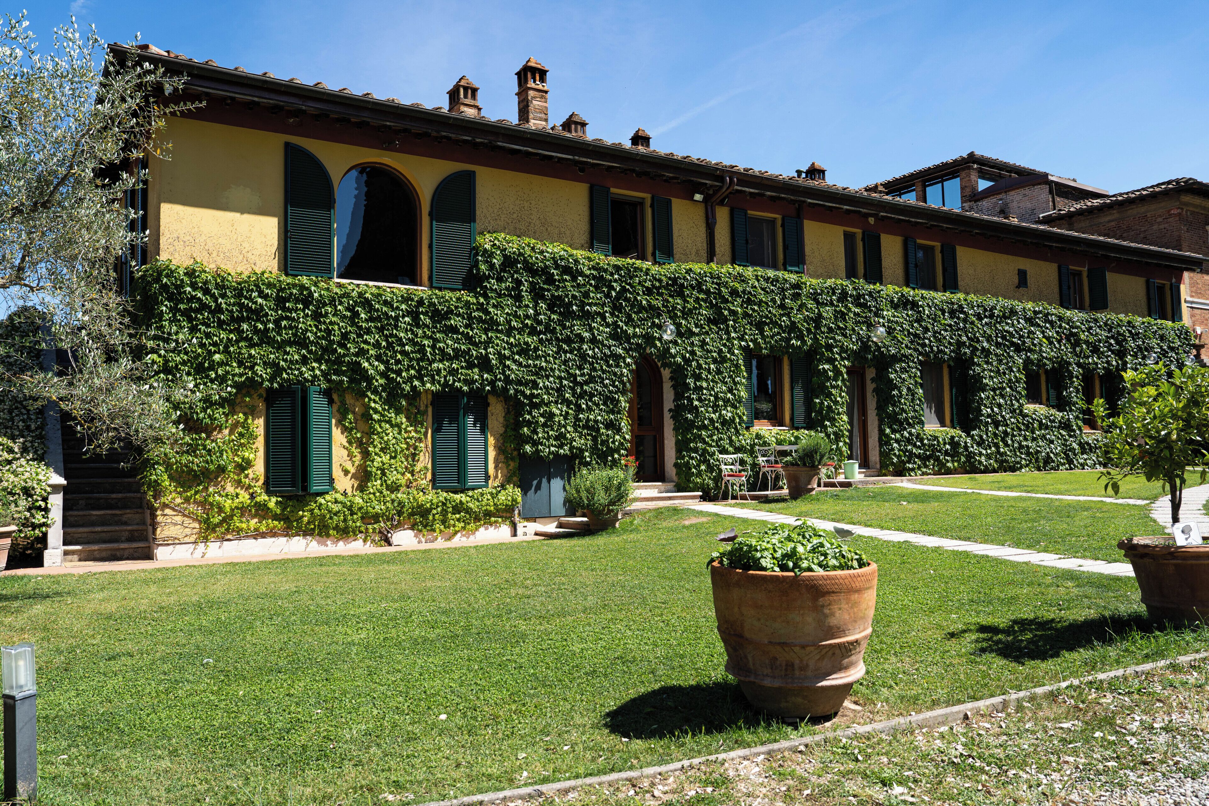 A building with a yellow facade, green shutters, and a garden area with potted plants.