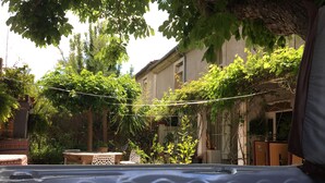 Ein Whirlpool in einem Garten mit einer Pergola darüber, umgeben von üppiger Bepflanzung und einem Gebäude im Hintergrund.