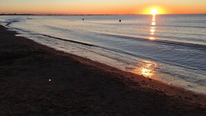 Ein Strand bei Sonnenuntergang mit ruhigem Wasser, das den Himmel spiegelt.
