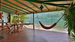 A wooden deck with a table and chairs, a hammock, and a view of a lake. - Beach Villa Cook - Robinson's Cove (Papetoai)