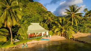 A beachfront property with a small house, a sandy beach, and palm trees. - Beach Villa Cook - Robinson's Cove (Papetoai)