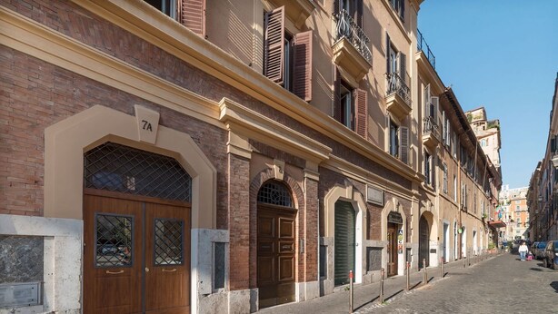 A street with a building featuring a large wooden door, a number '7A' sign, and a brick facade. - GuestHost - Cozy one bedroom apartment of about 55 sqm located on the ground floor of a building that can accommodate up to 4 people, perfect for visiting the wonders of the Eternal City! Just 100 meters far there is the stop of several urban bus lines,  (Roma)