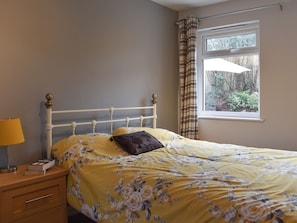 A bedroom with a bed, a bedside table, a lamp, and a window with curtains.