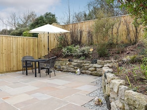 Eine Terrasse mit Steinplatten, ein Holzzaun und ein kleiner Gartenbereich mit einer Statue.