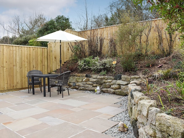 A patio with stone tiles, a wooden fence, and a small garden area with a statue.