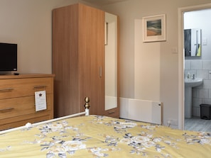 Une chambre à coucher avec un lit, une armoire en bois, un téléviseur posé sur une commode, et une salle de bain avec un lavabo et un miroir.