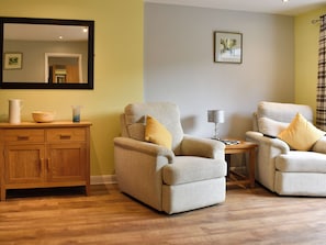 A living room with two armchairs, a wooden cabinet, and a mirror on the wall.