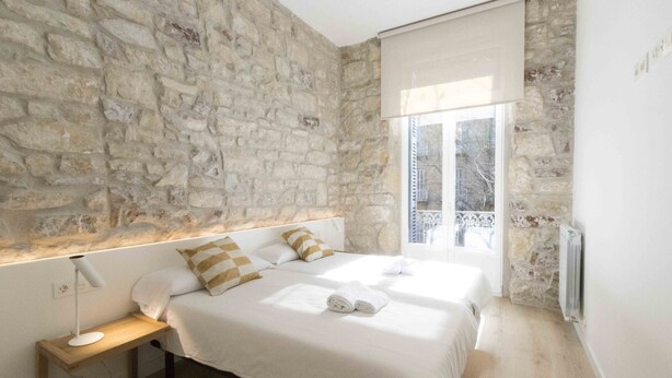 Un dormitorio con pared de piedra, dos camas, una mesita de noche y una ventana con vistas.
