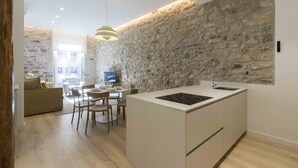 Una cocina moderna con pared de piedra, un área de comedor con sofá y sillas, y un televisor al fondo.