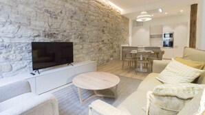 Una sala de estar moderna con una pared de piedra, un televisor de pantalla plana, una mesa de centro redonda y un sofá con cojines estampados.