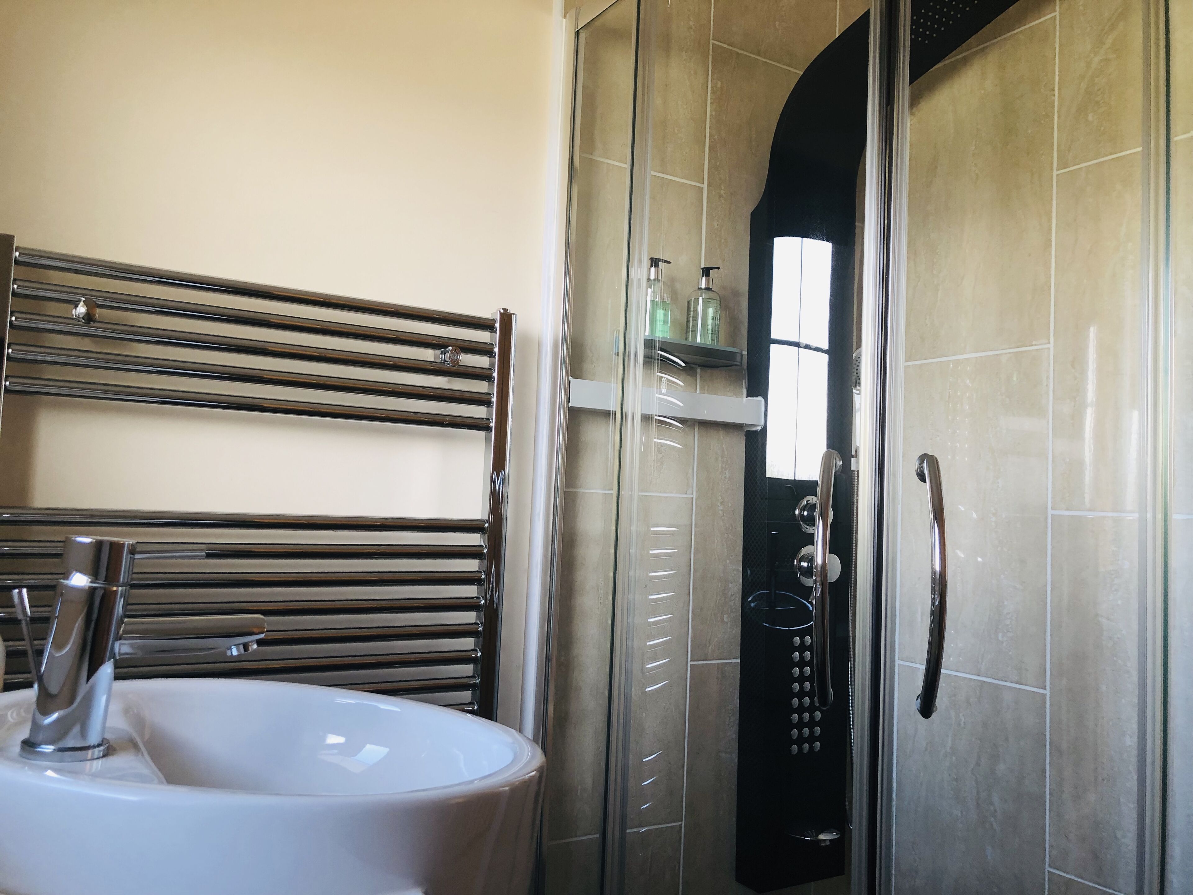 Een badkamer met een douche met glazen wand, een wit wastafelmeubel en een chromen handdoekrek.
