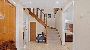 A spacious hallway with a wooden staircase, a bench, and a door leading to a room with a bed. - Taigh d'Luxe - Classic elegance meets modern chic in stunning spacious villa (Inverness)