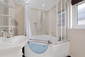 Een bad/douchecombinatie, een bubbelbad, een haardroger, handdoeken