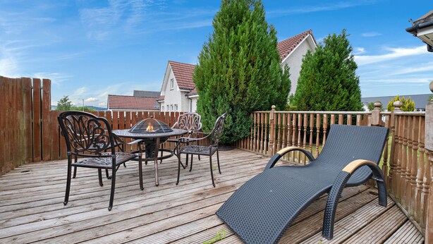 A wooden deck with a table and chairs, a lounge chair, and a fire pit. - Taigh d'Luxe - Classic elegance meets modern chic in stunning spacious villa (Inverness)
