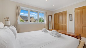 A hotel room with a large bed, a wooden bench, a mirror, and a window with curtains. - Taigh d'Luxe - Classic elegance meets modern chic in stunning spacious villa (Inverness)