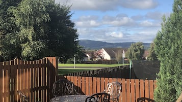 Relax in a serene patio setting surrounded by lush greenery and distant hills.