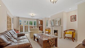 A living room with a brown leather sofa, a beige armchair, a wooden coffee table, and a yellow armchair. There is a fireplace with a mantel and a framed picture above it. - Taigh d'Luxe - Classic elegance meets modern chic in stunning spacious villa (Inverness)