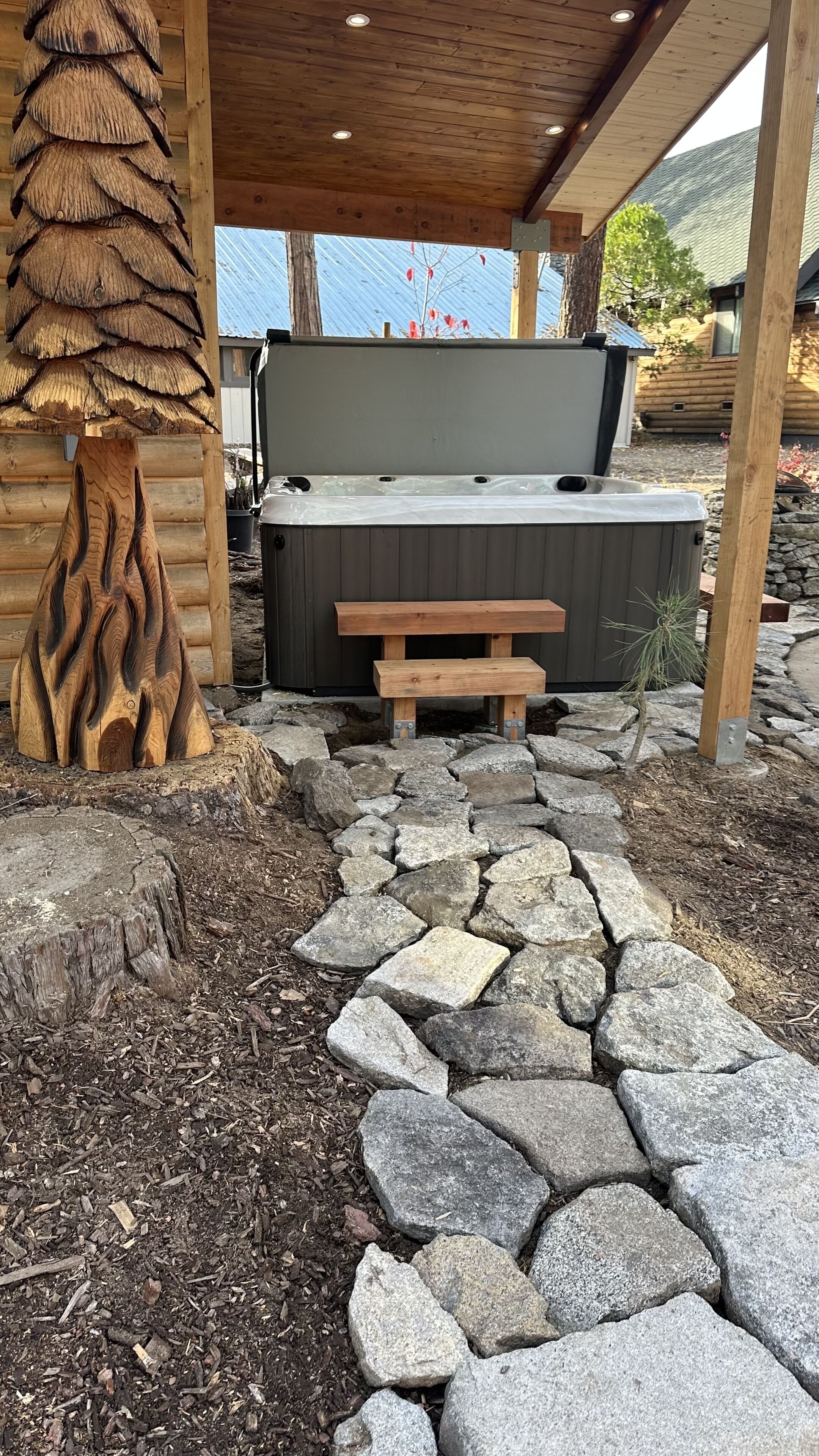 A wooden deck with a stone pathway leading to a hot tub and a wooden bench.