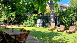 A backyard with a wooden table and chairs, a grassy lawn, and a tree providing shade. - Pet Friendly - Elwood Eclectic Gem Walk to St Kilda beach - Flexible Home offering 4 or 6 Bedrooms. (Elwood)