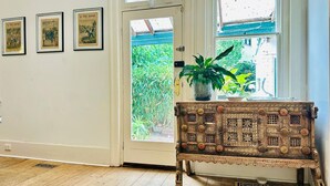 A room with a wooden door, a small table with a plant, and three framed pictures on the wall. - Pet Friendly - Elwood Eclectic Gem Walk to St Kilda beach - Flexible Home offering 4 or 6 Bedrooms. (Elwood)