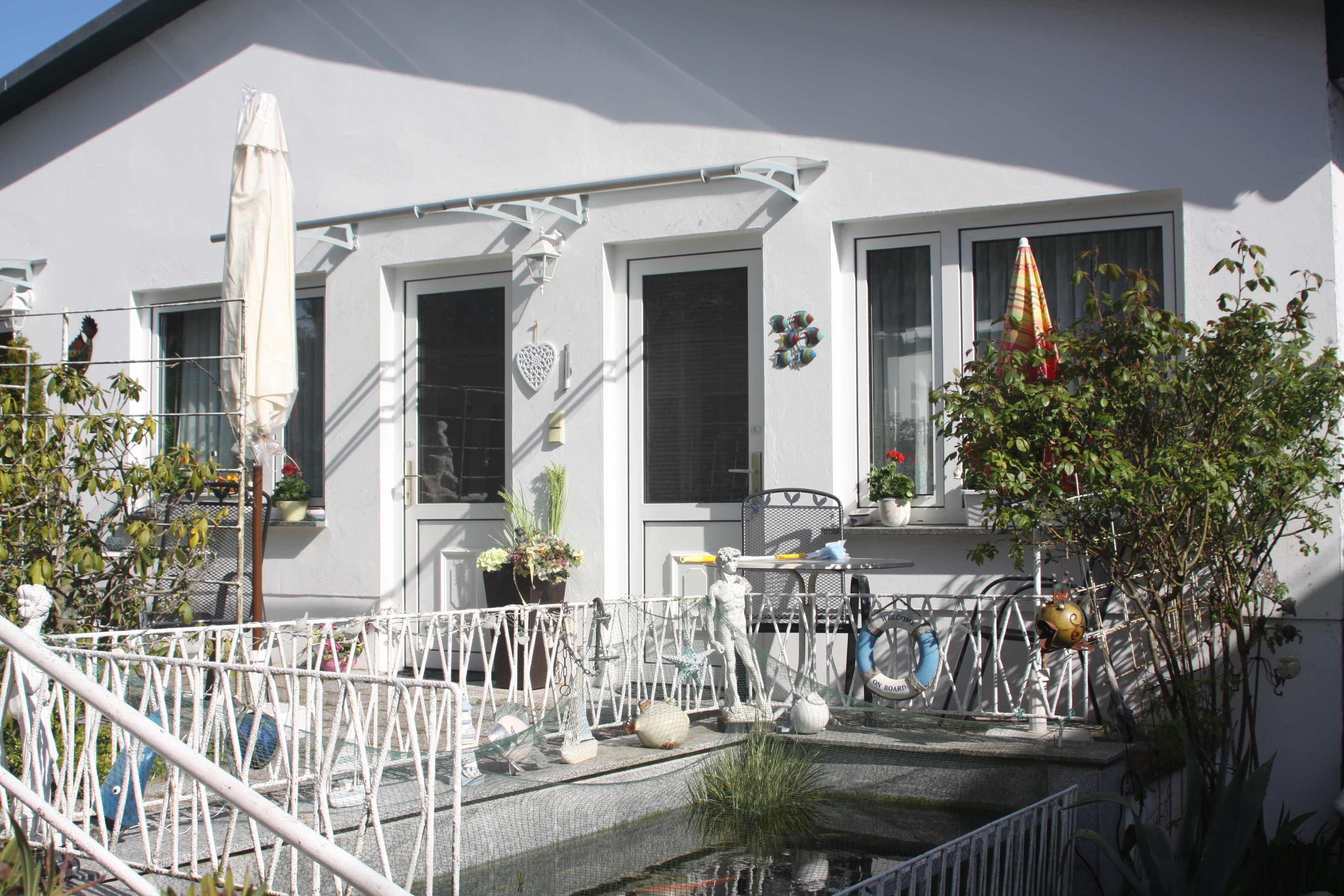 Un edificio bianco con numerose finestre, una zona relax all'aperto coperta, e diverse decorazioni esterne tra cui una statua, una bicicletta e un piccolo giardino.