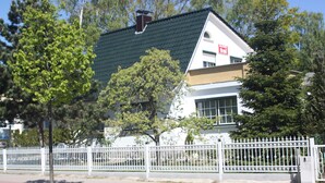 Um edifício de dois andares com telhado verde, paredes brancas e cerca branca na frente.