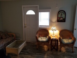 Cozy living room with a traditional design, featuring a wicker chair, small table, and framed picture on the wall.