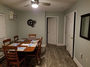 A dining room with a table for four, ceiling fan, air conditioning unit, and decorative clock.