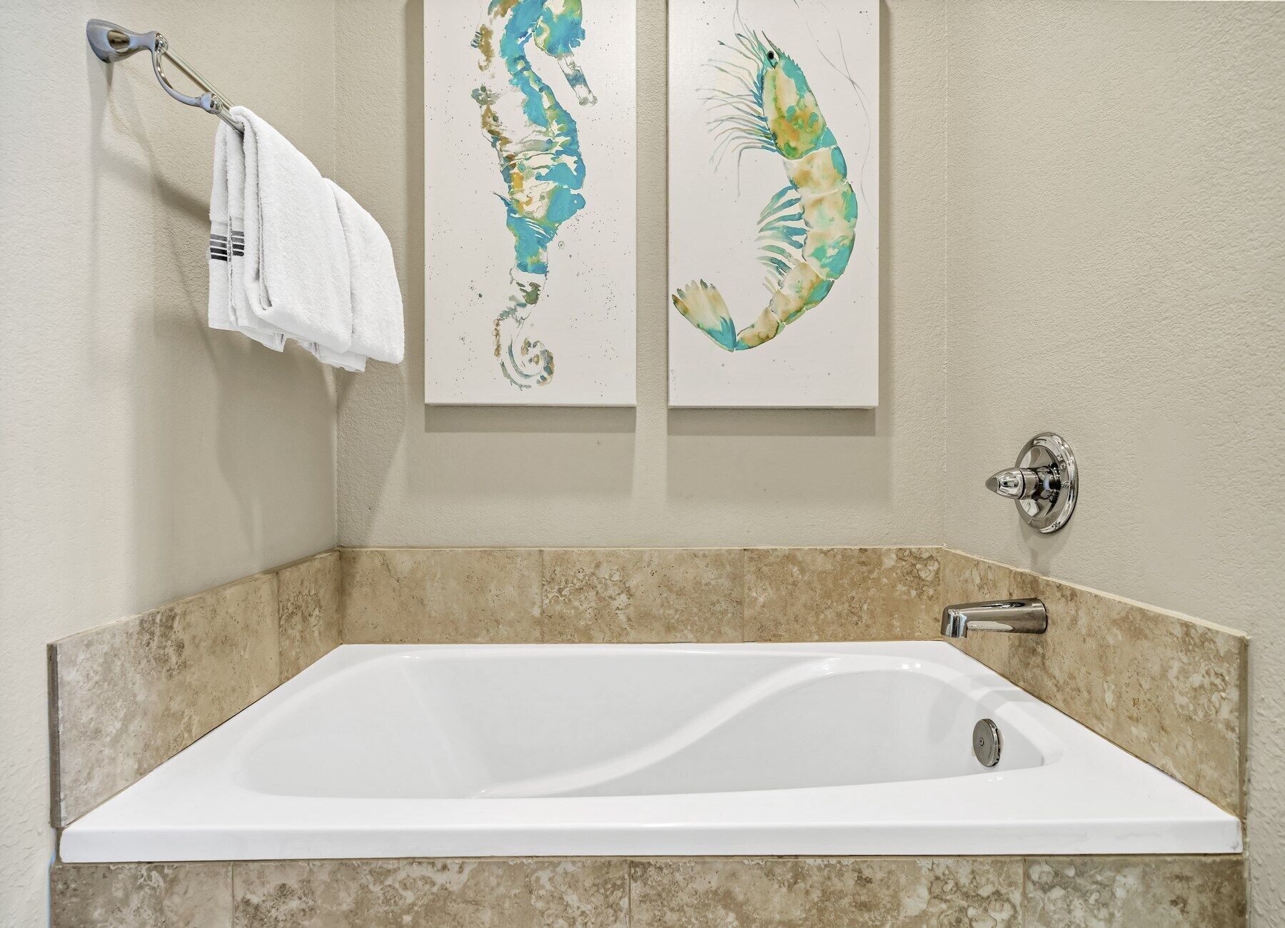 A bathroom with a white bathtub, beige tiles, and two wall-mounted artwork pieces.