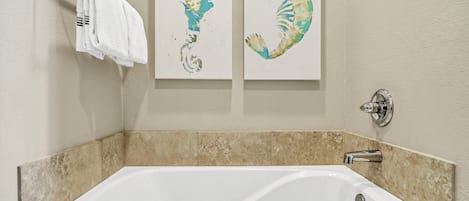 A bathroom with a white bathtub, beige tiles, and two wall-mounted artwork pieces.