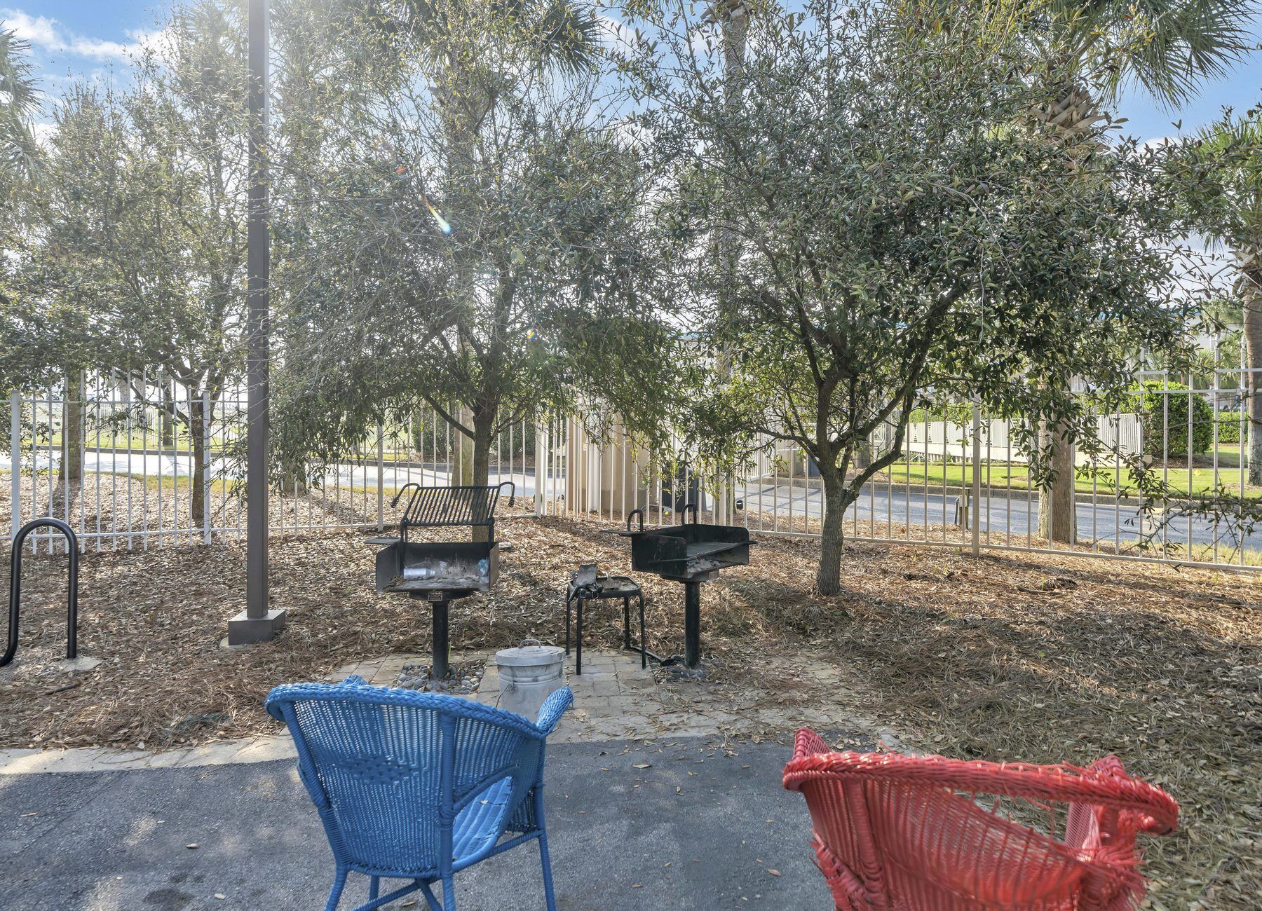 Un parc doté d’une allée pavée, de bancs en métal et d’un fauteuil tressé aux couleurs bleu et rouge.