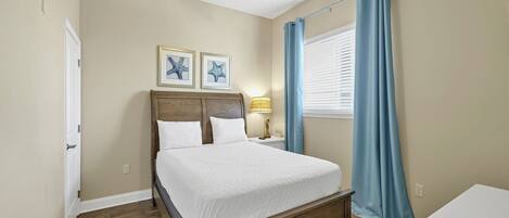 A bedroom with a wooden bed, a ceiling fan, a nightstand with a lamp, and two framed pictures on the wall.