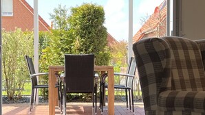 Un patio con mesa y sillas, techo de cristal y vista a un barrio residencial con casas y árboles.