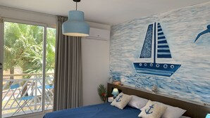 Un dormitorio con un ventanal grande, una cama con ropa de cama azul, una lámpara en el techo y un mural en la pared de un velero.