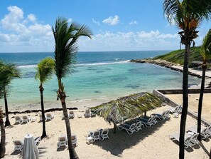 Une plage avec des chaises longues et des tables blanches, des palmiers et une vue sur l’océan.