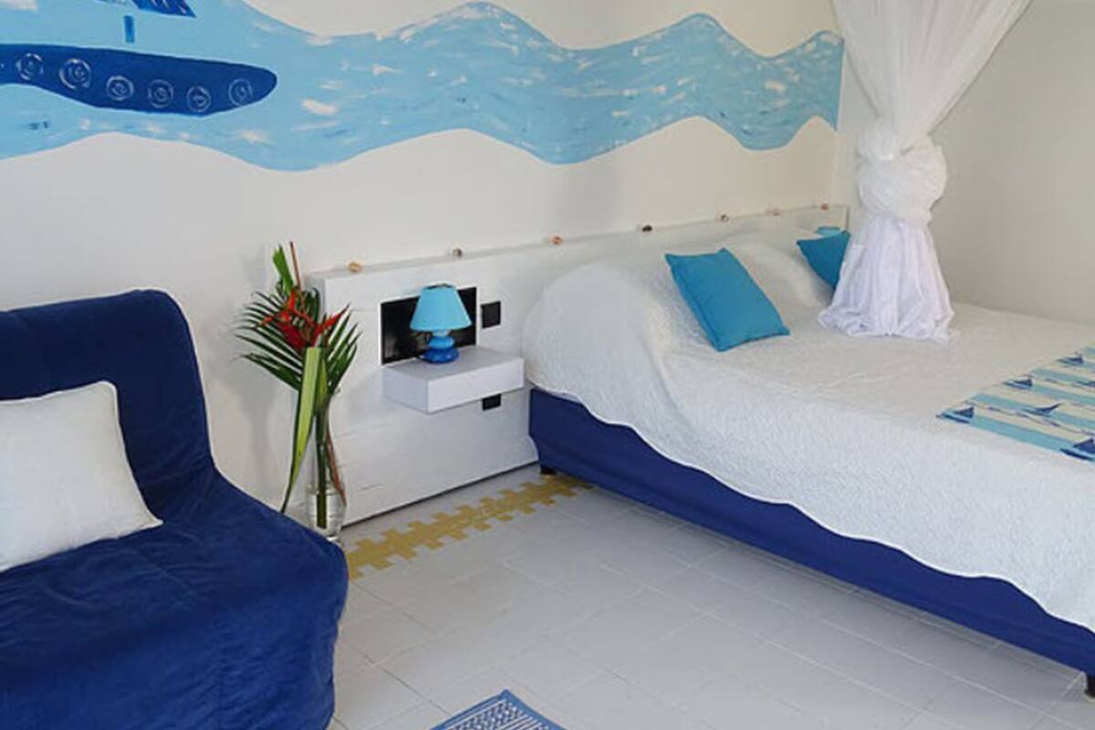 Un dormitorio con una cama, una mesita de noche, una silla azul y un mural en la pared.