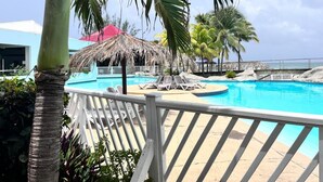 Un área de piscina con sillones de descanso, una sombrilla de paja y palmeras.