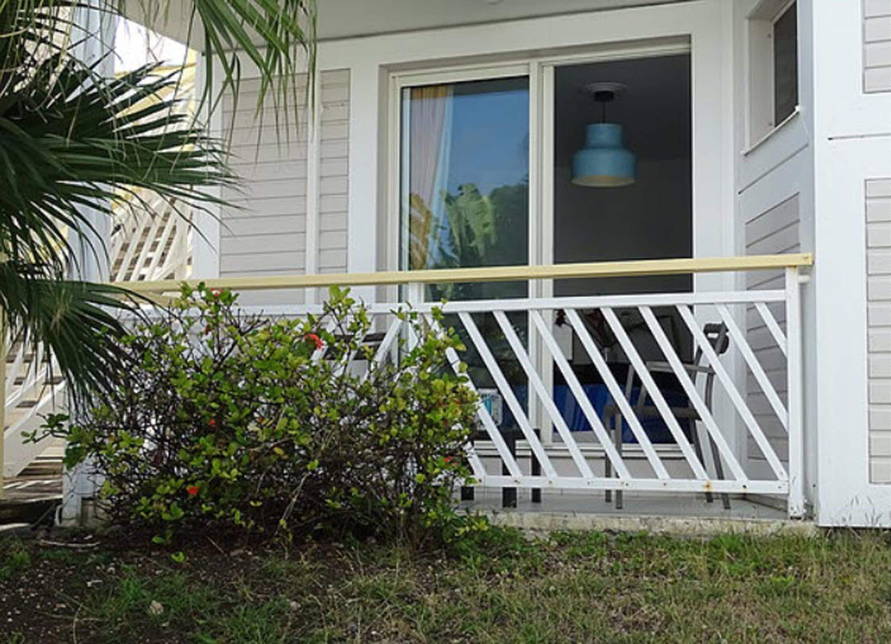 A white house with a covered porch, a small garden, and a window with a curtain.