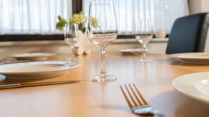Een eettafel gedekt met borden, bestek en wijnglazen, met een raam en gordijnen op de achtergrond.
