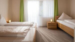 Een hotelkamer met een houten plafond, twee bedden met witte lakens, groene gordijnen en een nachtkastje met een lamp.