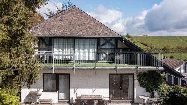 Een huis met twee verdiepingen, een balkon, een stenen terras en een zithoek buiten.