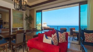 A spacious living area with a red sofa, a dining table, and chairs. There is a large window offering a view of the sea. - LUXURIOUS PRESIDENTIAL suite 2 bedroom 3 baths (Cabo San Lucas)