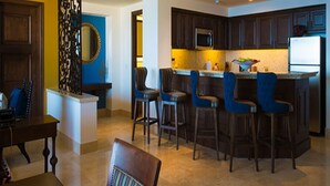 A modern kitchen with dark wooden cabinets, a central island with bar stools, and a microwave above the island. - LUXURIOUS PRESIDENTIAL suite 2 bedroom 3 baths (Cabo San Lucas)