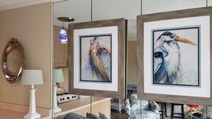 Una habitación con dos cuadros enmarcados de pájaros, una lámpara blanca y una zona de cocina con estufa y armarios.