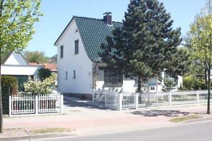 A white building with a green roof, surrounded by a white fence, and trees in the foreground.
