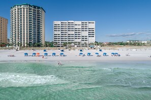 A beach with clear turquoise water, a sandy shore, and several blue umbrellas.