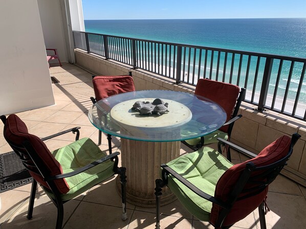 A glass-top table with chairs on a balcony overlooking the ocean.