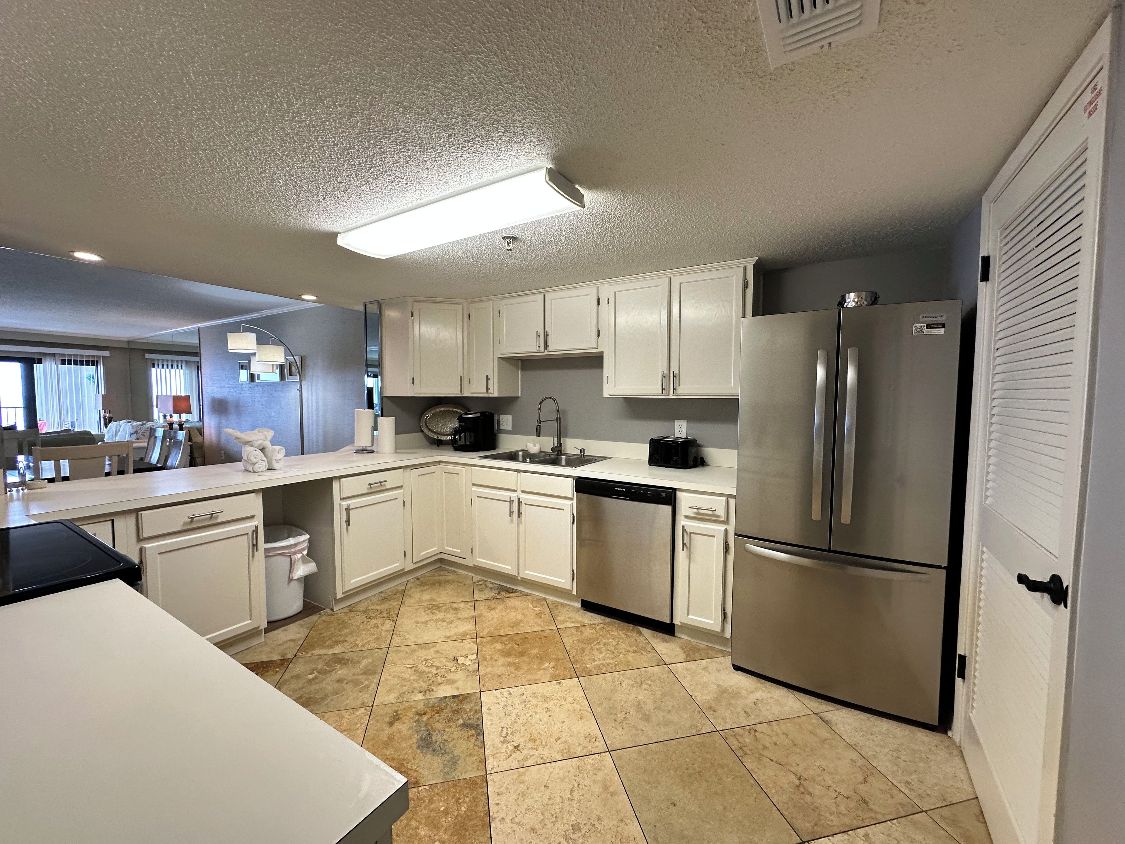 A modern kitchen with white cabinets, a stainless steel refrigerator, a dishwasher, and a coffee maker.