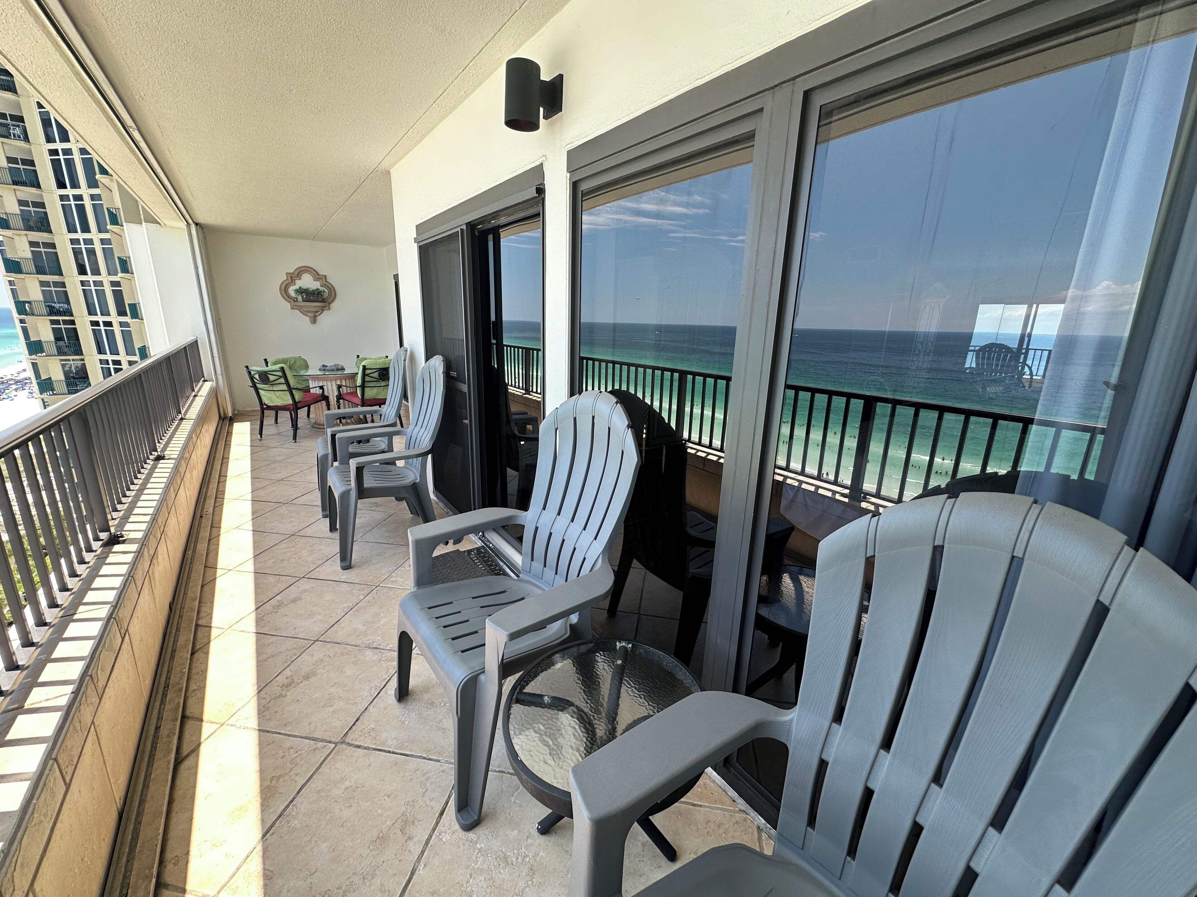 A balcony with chairs and tables, overlooking a beach with a clear view of the ocean.