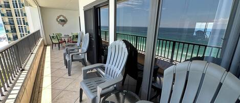 A balcony with chairs and tables, overlooking a beach with a clear view of the ocean.